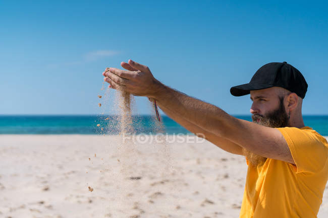 Homem derramando areia na praia — Fotografia de Stock