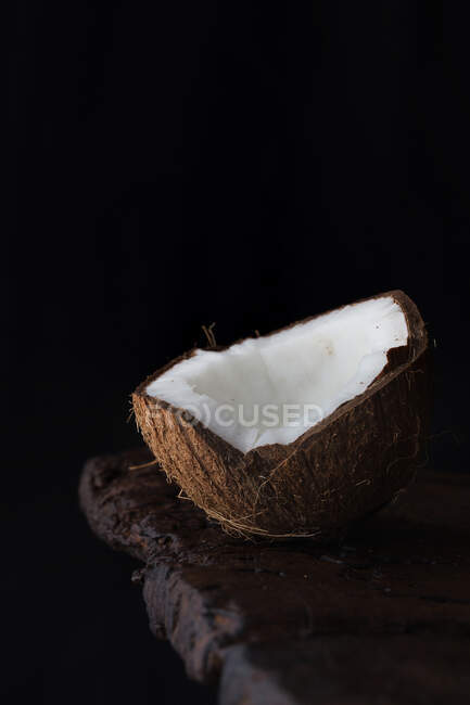 Close-up of ripe aromatic coconut half on rough wooden table against black background. — Stock Photo