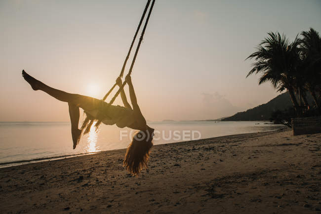 Woman swinging on beach in sunset — Stock Photo
