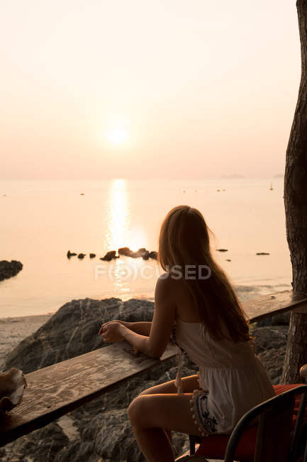 Frau blickt auf Sonnenuntergang am felsigen Strand — Stockfoto