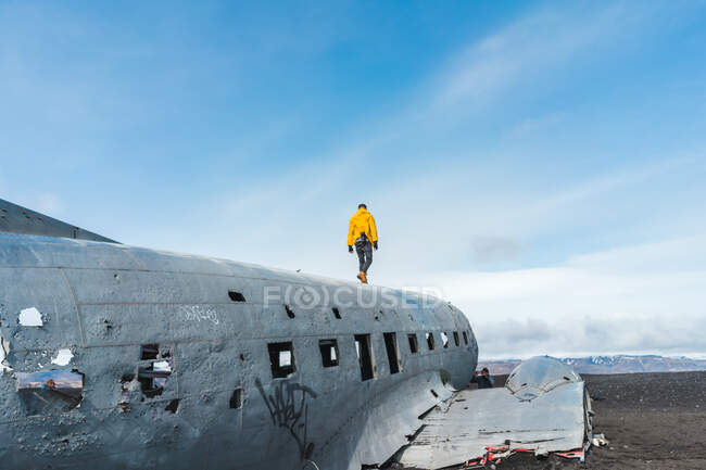 Faceless young man walking on carcass of abandoned aircraft while traveling through Iceland — Stock Photo