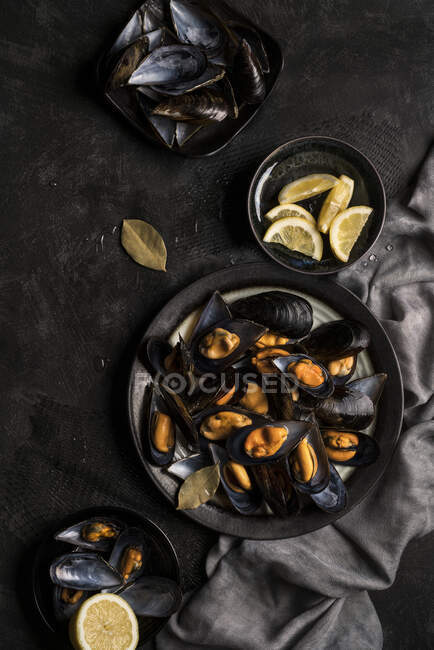 Vista superior de mejillones apetitosos recién horneados servidos con limón sobre una mesa oscura. - foto de stock