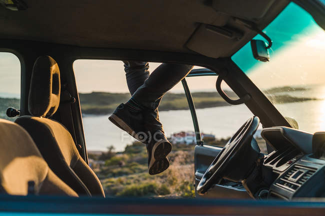 Human legs sitting on car roof — Stock Photo