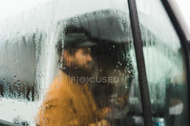 Adult man shot from behind wet car window while standing on street in rainy day in Iceland — Stock Photo