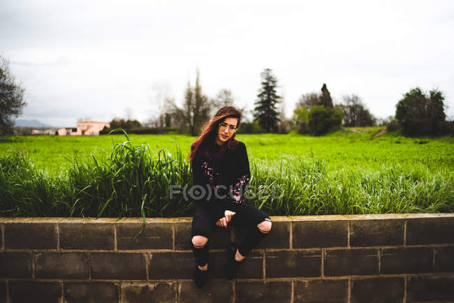 Женщина сидит на кирпичной стене в сельской местности — стоковое фото