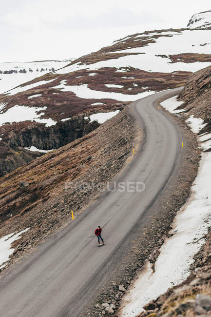 Vista aérea do viajante andar de skate em estrada remota longa em montanhas nevadas da Islândia. — Fotografia de Stock