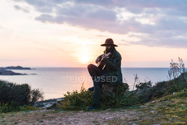 Uomo seduto con la chitarra sulla costa — Foto stock