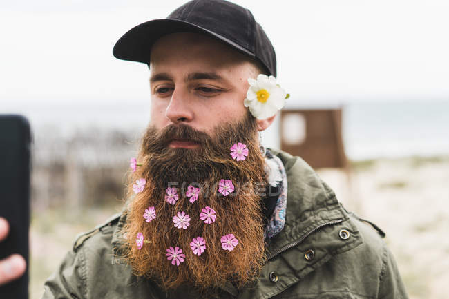Человек с цветами в бороде делает селфи — стоковое фото