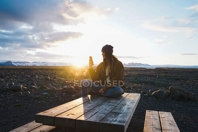 Женщина, сидящая на деревянном столе на закате — стоковое фото