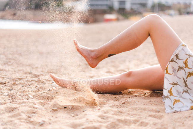 Jambes féminines coups de pied sable sur la plage — Photo de stock