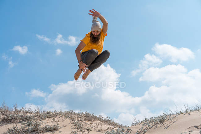 Чоловік стрибає на піщаному пагорбі — стокове фото