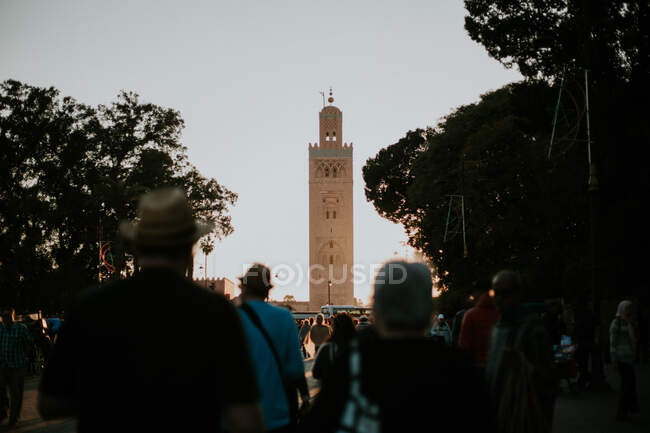 Back view of tourists looking at tall tower landmark in Morocco. — Stock Photo