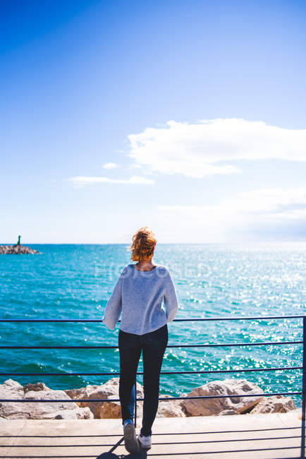 Femme debout à la main courante et regardant l'océan — Photo de stock