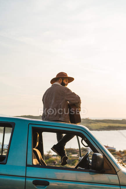 Uomo seduto sul tetto dell'auto al mare — Foto stock