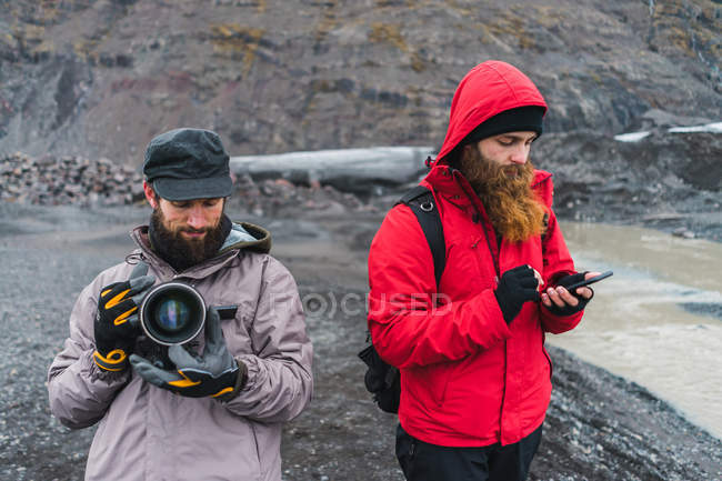 Hombres en ropa de abrigo usando dispositivos en la naturaleza - foto de stock