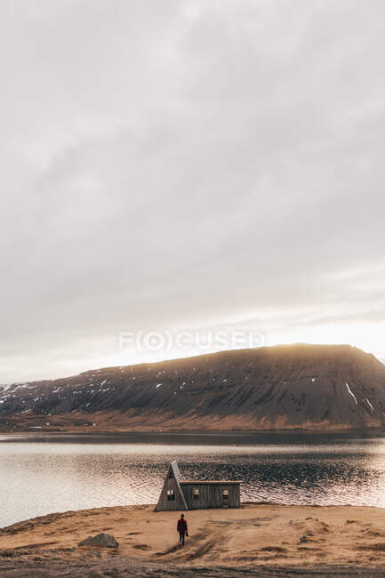 Paisagem de lago remoto e casa na costa com o homem andando sozinho ao pôr do sol, Islândia. — Fotografia de Stock