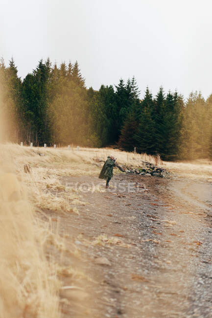 Side view of anonymous person standing on gray pebbled beach of shoreline with evergreen forest on background. — Stock Photo