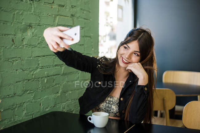 Женщина сидит в кафе и делает селфи — стоковое фото