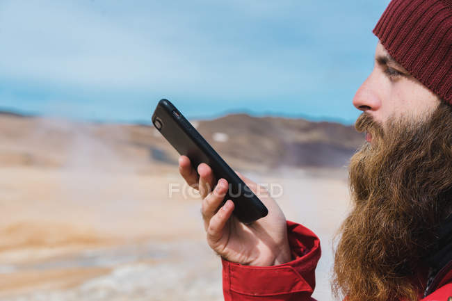 Человек, стоящий со смартфоном у гейзера — стоковое фото