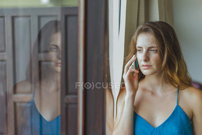 Frau telefoniert am Fenster mit Handy — Stockfoto