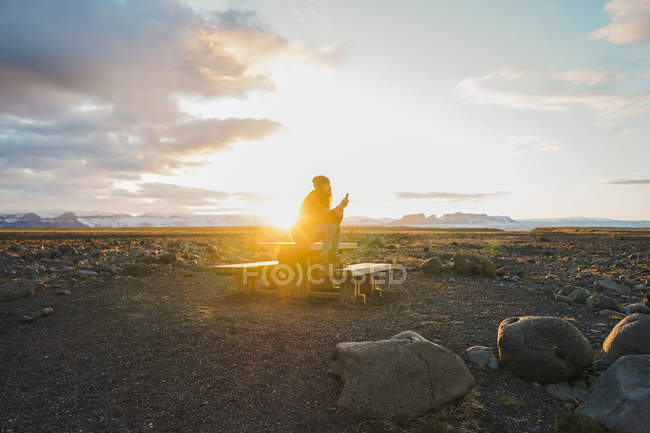 Жінка сидить на дерев'яному столі на заході сонця — стокове фото