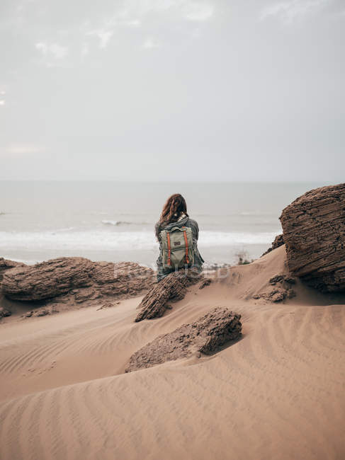 Женщина с рюкзаком сидит на скале — стоковое фото