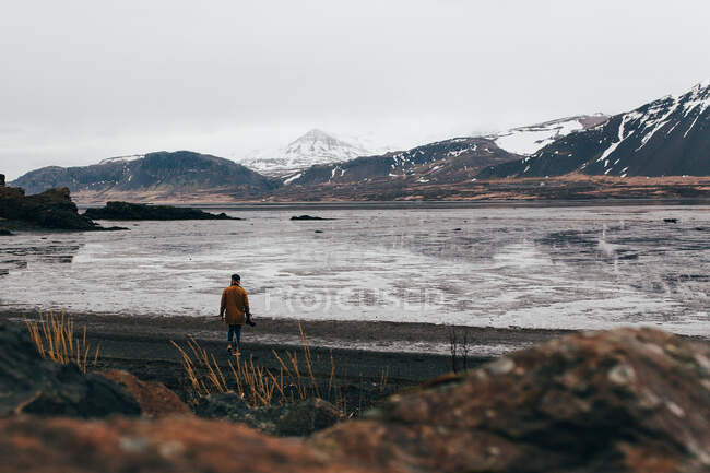Blick auf eine Person am Ufer des zugefrorenen Sees mit Bergen im Hintergrund, Island. — Stockfoto