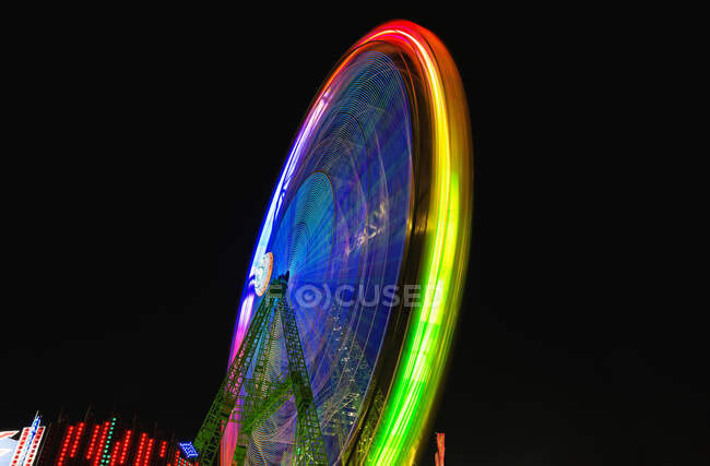 Tracce di luci colorate sulla ruota panoramica in movimento sullo sfondo del cielo notturno scuro. — Foto stock
