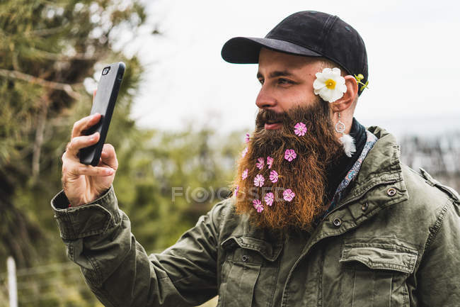Человек с цветами в бороде делает селфи — стоковое фото