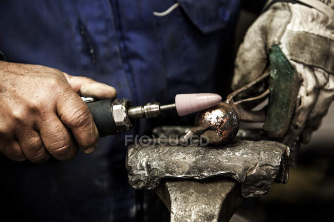 Crop close-up view of blacksmith hands treating iron ball on anvil — Stock Photo