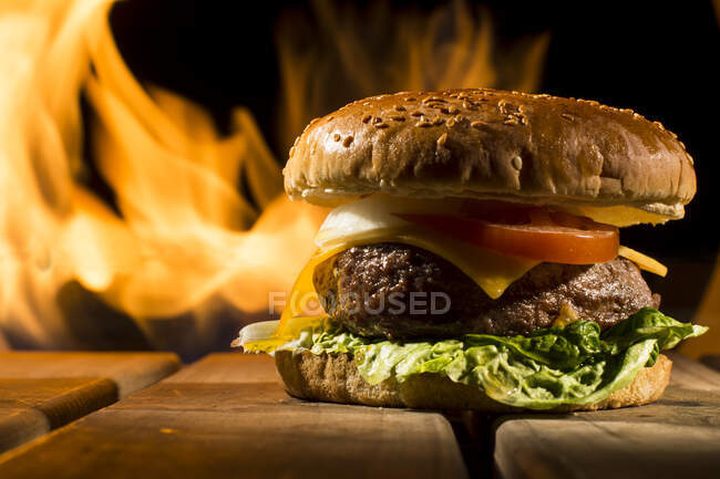 Tasty burger with large chop lying on wooden table on the background of fire — Stock Photo