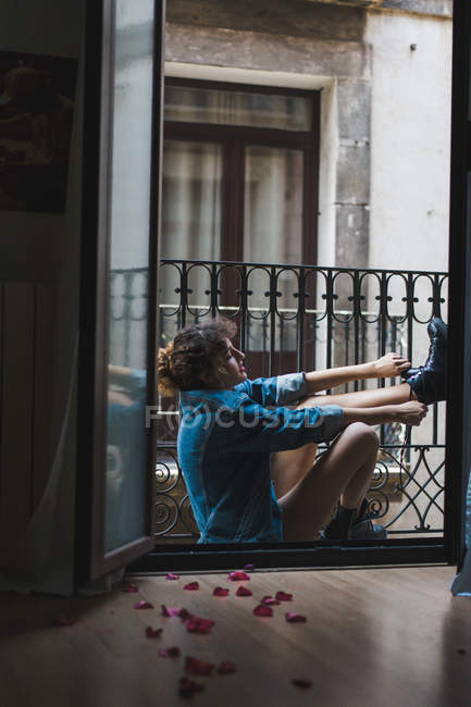 Woman putting on boots on balcony — Stock Photo