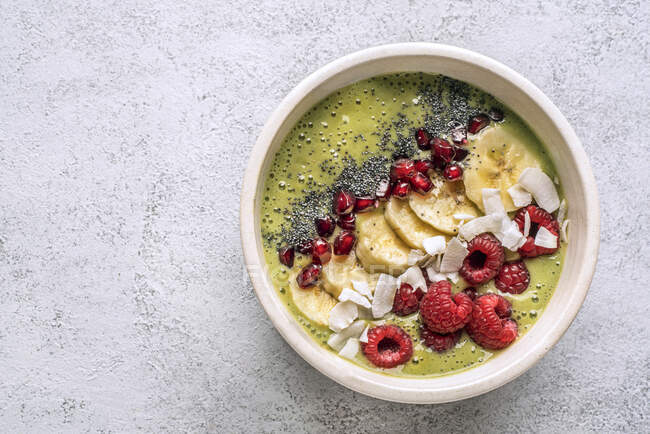From above view of bowl with green smoothie garnished with various seeds and berries with banana. — Stock Photo