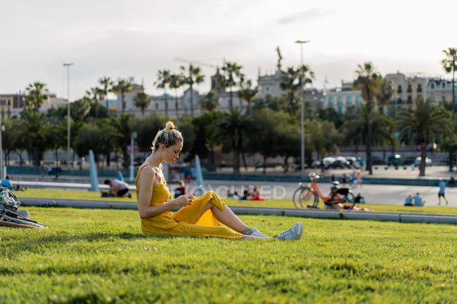 Mujer sentada en la hierba con smartphone - foto de stock
