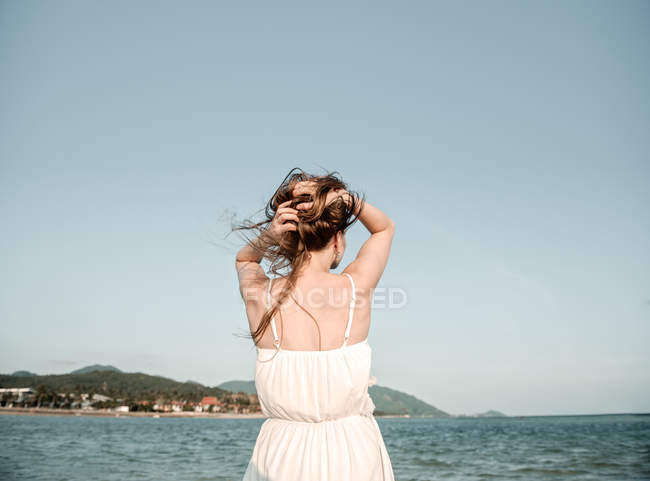 Femme ajustement des cheveux au bord de la mer — Photo de stock