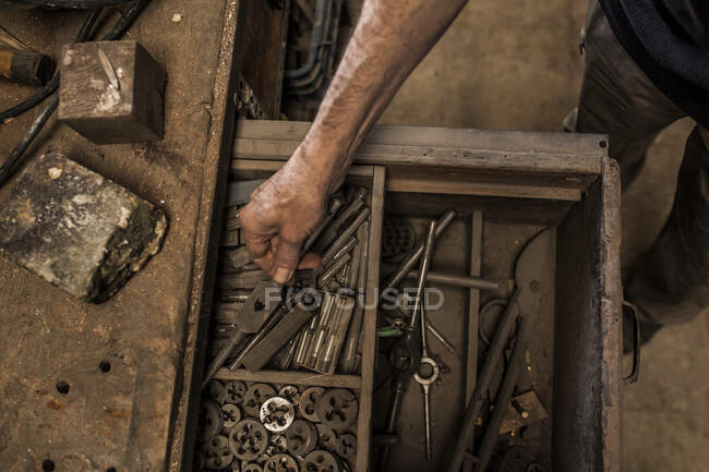 Vista de la cosecha desde arriba de las manos del hombre toma el instrumento de la caja abierta de mesa de madera con herramientas de carpintería - foto de stock