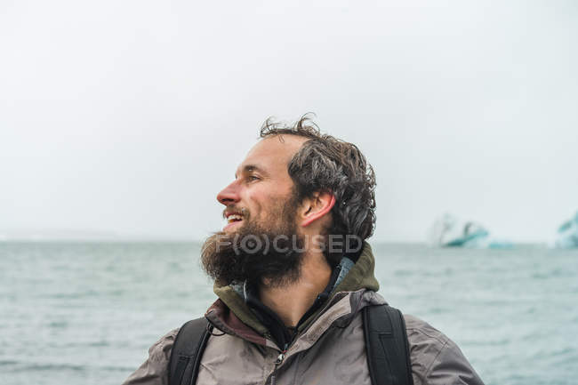 Homem barbudo com mochila de pé no mar — Fotografia de Stock