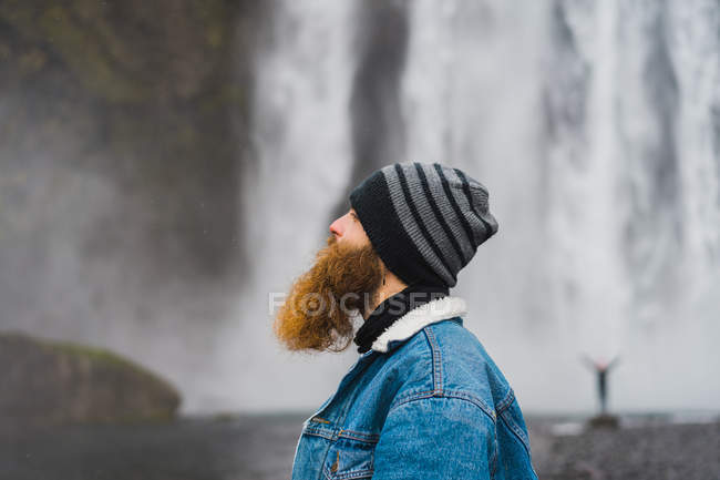 Hombre de pie frente a la cascada - foto de stock