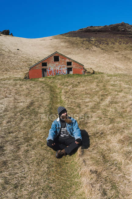 Homme assis devant une petite maison — Photo de stock