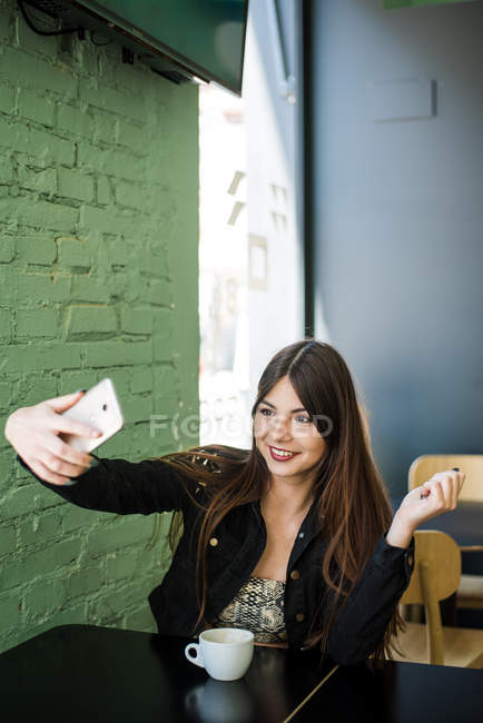 Young beautiful lady sitting in cafe and making selfie — Stock Photo