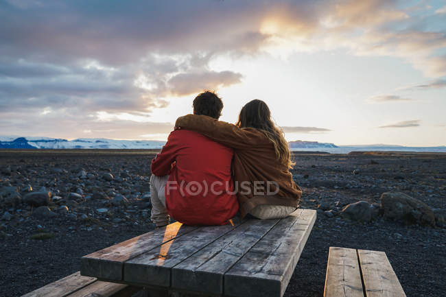 Пара сидящая на деревянном столе на закате — стоковое фото