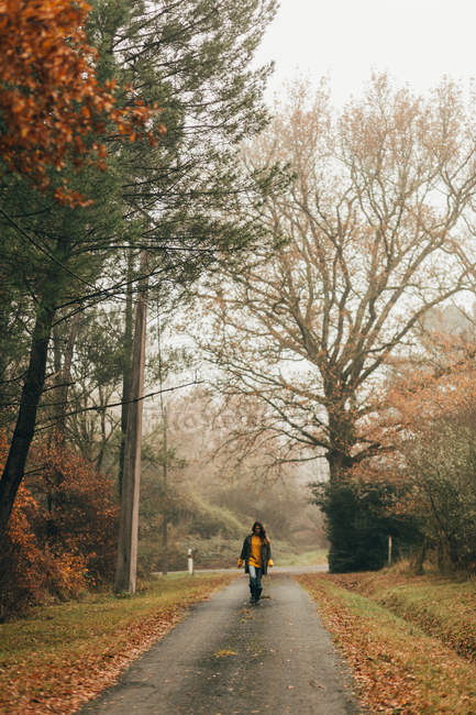 Femme marchant sur la route dans les bois d'automne — Photo de stock