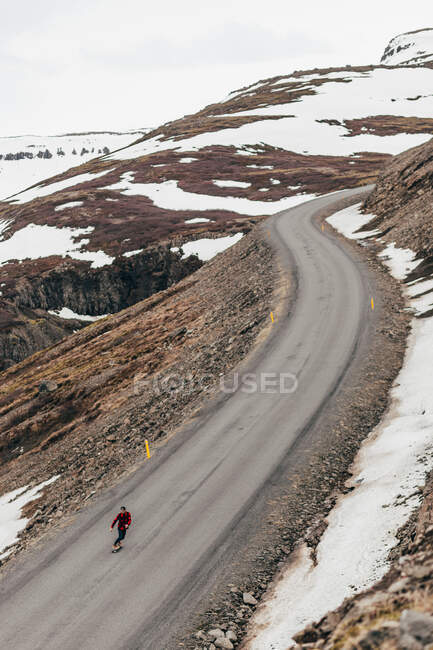 Vue aérienne du voyageur qui skate sur une longue route reculée dans les montagnes enneigées d'Islande. — Photo de stock
