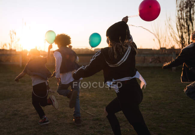 Bambini in esecuzione giocoso con palloncini al tramonto — Foto stock