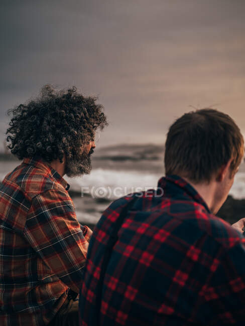 Двое взрослых мужчин сидят у океана в облачный вечер. — стоковое фото