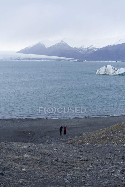Двоє людей стоять на березі мальовничого гірського озера в Скафтафеллі (Ісландія) і Ватнайокутлі. — стокове фото