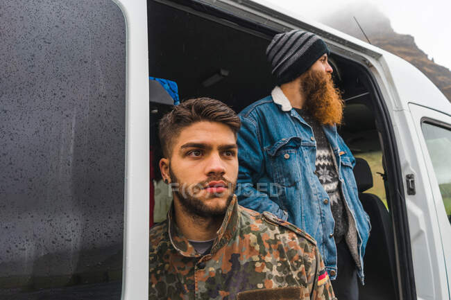 Deux jeunes hommes debout près d'un joli van blanc tout en voyageant à travers la magnifique campagne islandaise — Photo de stock