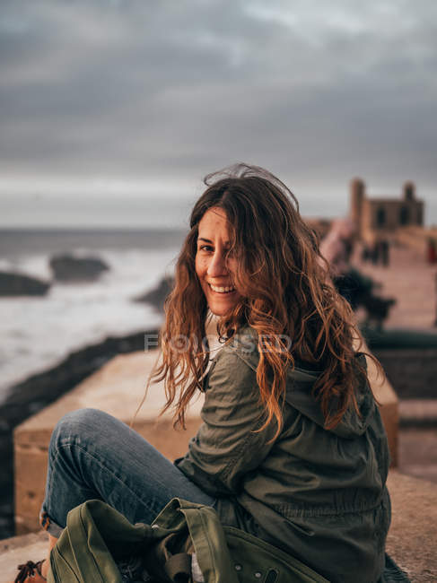 Mujer sonriente sentada a la orilla del mar - foto de stock