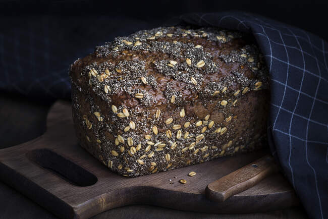 Loaf of tasty fresh baked rye bread with seeds on wooden board. — Stock Photo