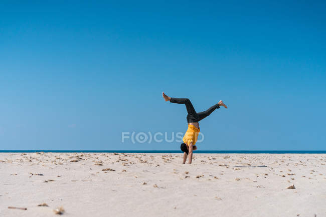 Человек делает стойку на руках на песчаном пляже — стоковое фото
